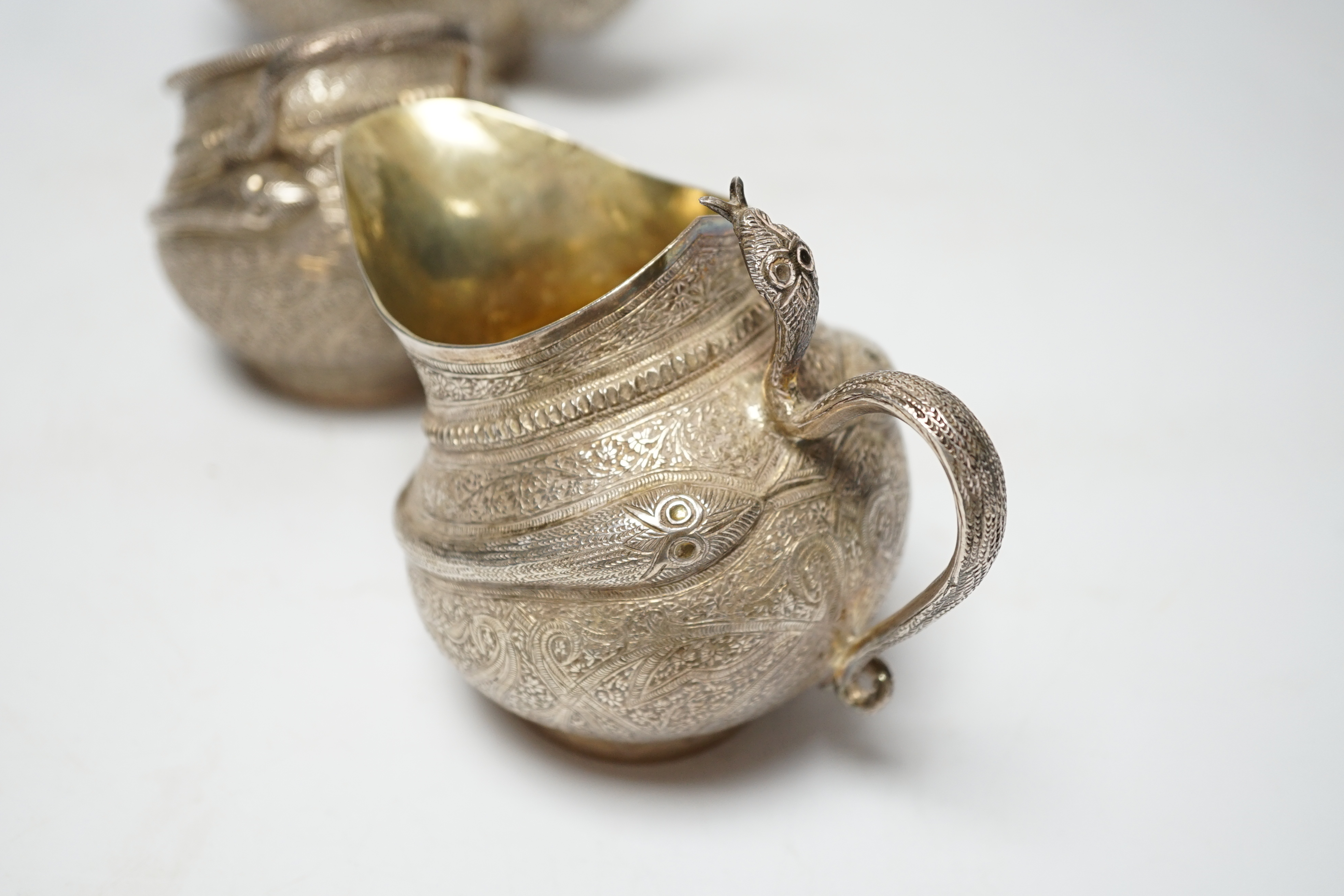 A 20th century Indian three piece embossed white metal tea set, with boteh and cobra decoration, gross weight 38.6oz.
